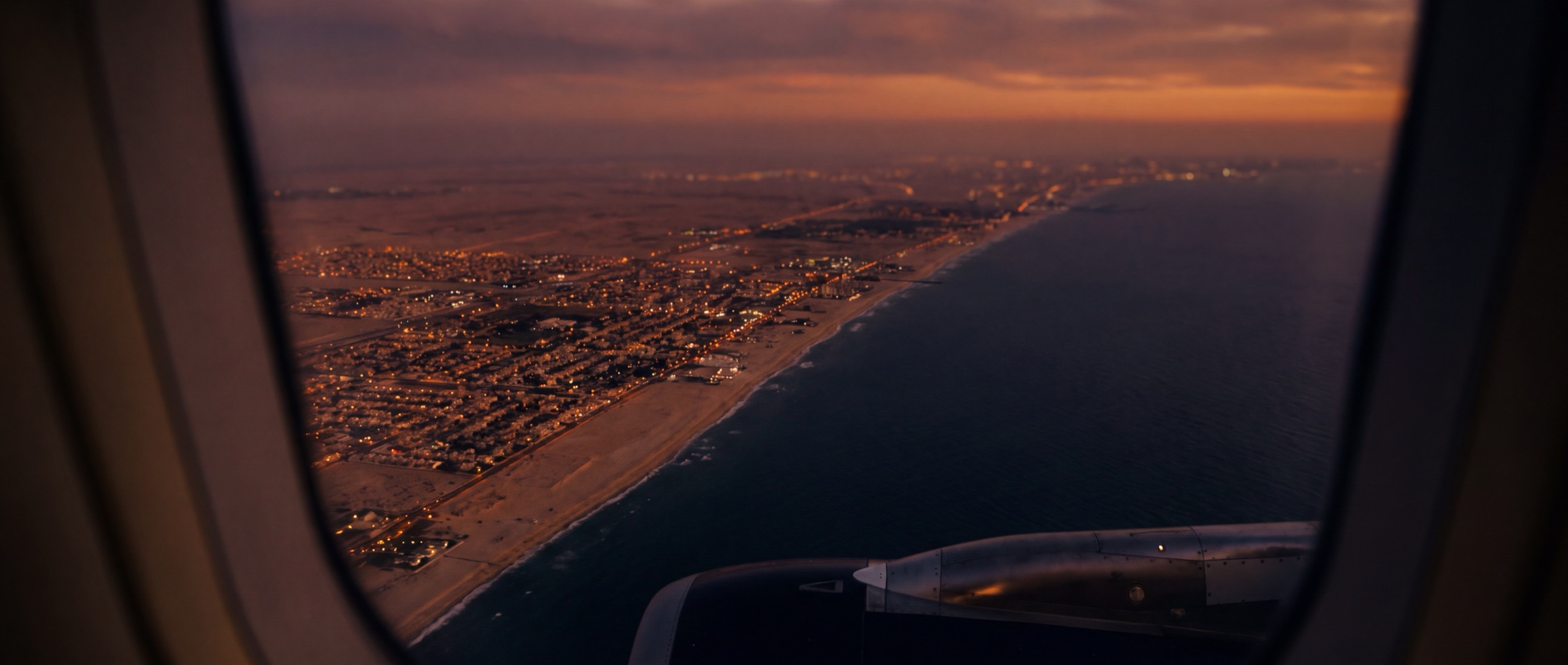 Aerial view from an aircraft window on approach over a coastline city at dusk