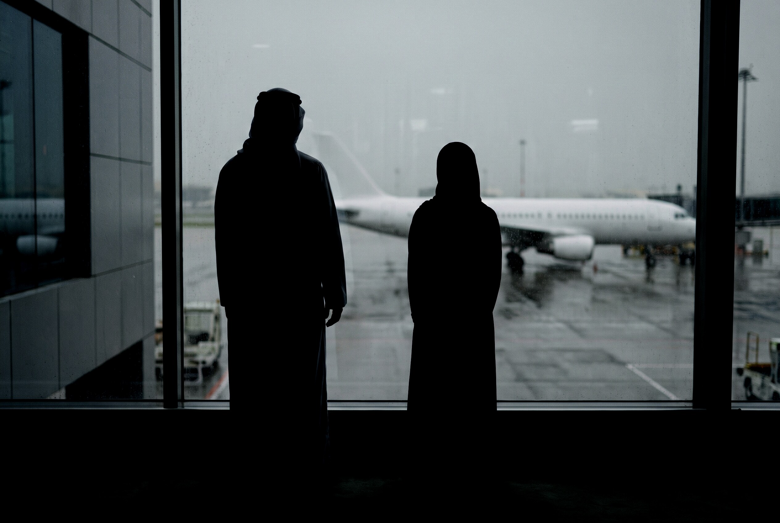 An Emirati father and his teenage daughter at the terminal glass, an aircraft on the apron beyond